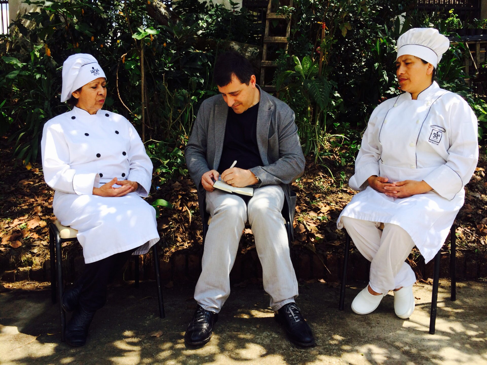 Fotografía de J Roca, tomando nota bajo un árbol de aguacate de las enseñanzas de Selmira y Fabiana, dos cocineras instructoras en SENA en la localidad de Río Negro, Antioquia, Colombia