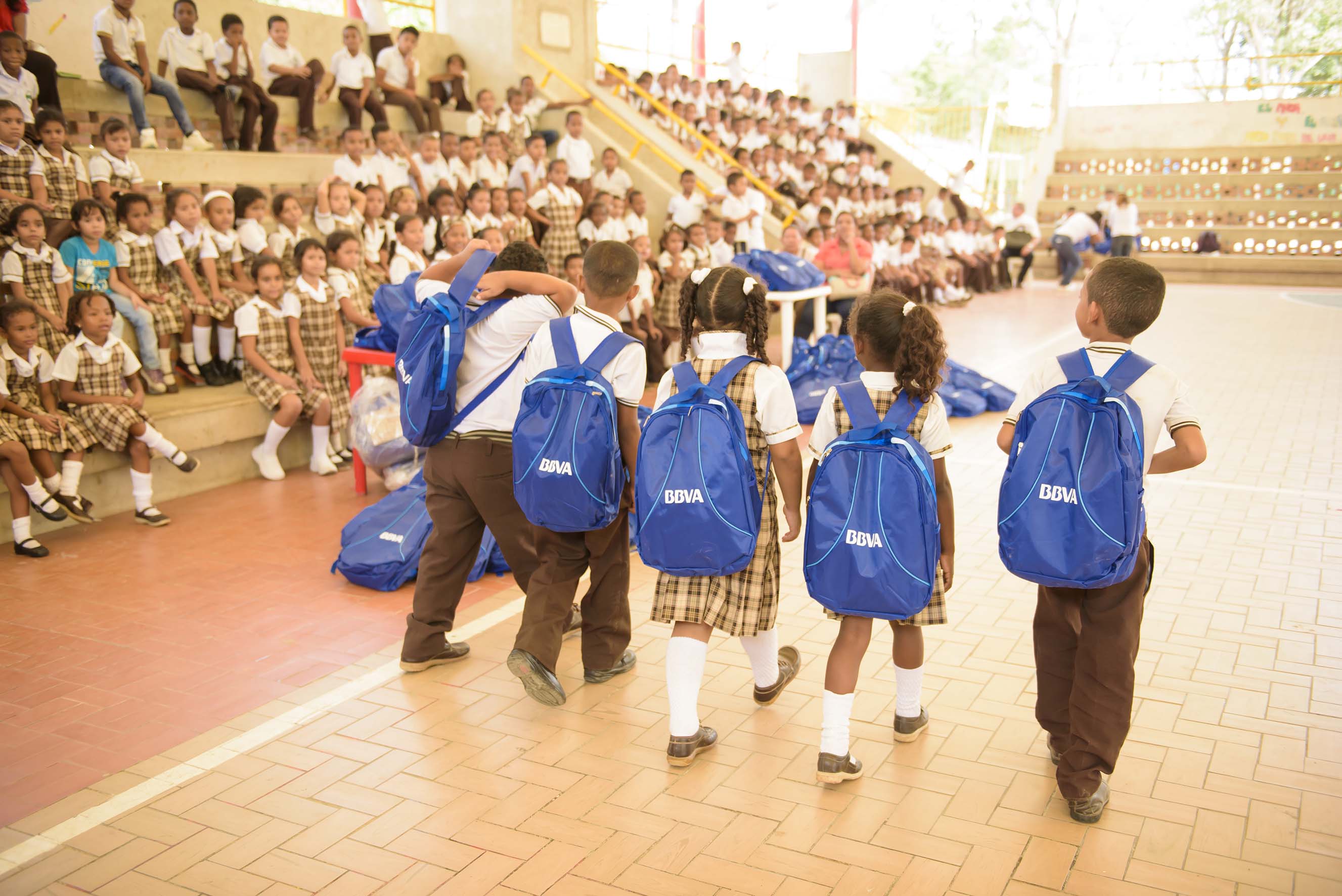 Niños caminan con morrales que tienen elementos escolares donados por BBVA Fotografía de niños caminando con morrales donados por BBVA con elementos escolares