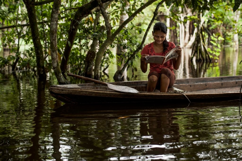 Estudiante en una balsa en Iquitos con libro del programa Fotografía de estudiante del programa