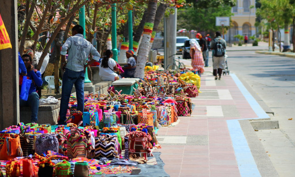 Foto de una calle de Colombia donde un grupo de personas venden mochilas, bolsos y hamacas tejidos a mano Foto de una calle de Colombia donde un grupo de personas venden mochilas, bolsos y hamacas tejidos a mano - Fundación Microfinanzas BBVA