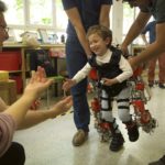 Imagen de Álvaro, de cinco años y afectado por atrofia muscular espinal, camina hacia sus padres durante una prueba del exoesqueleto. / Joan Costa