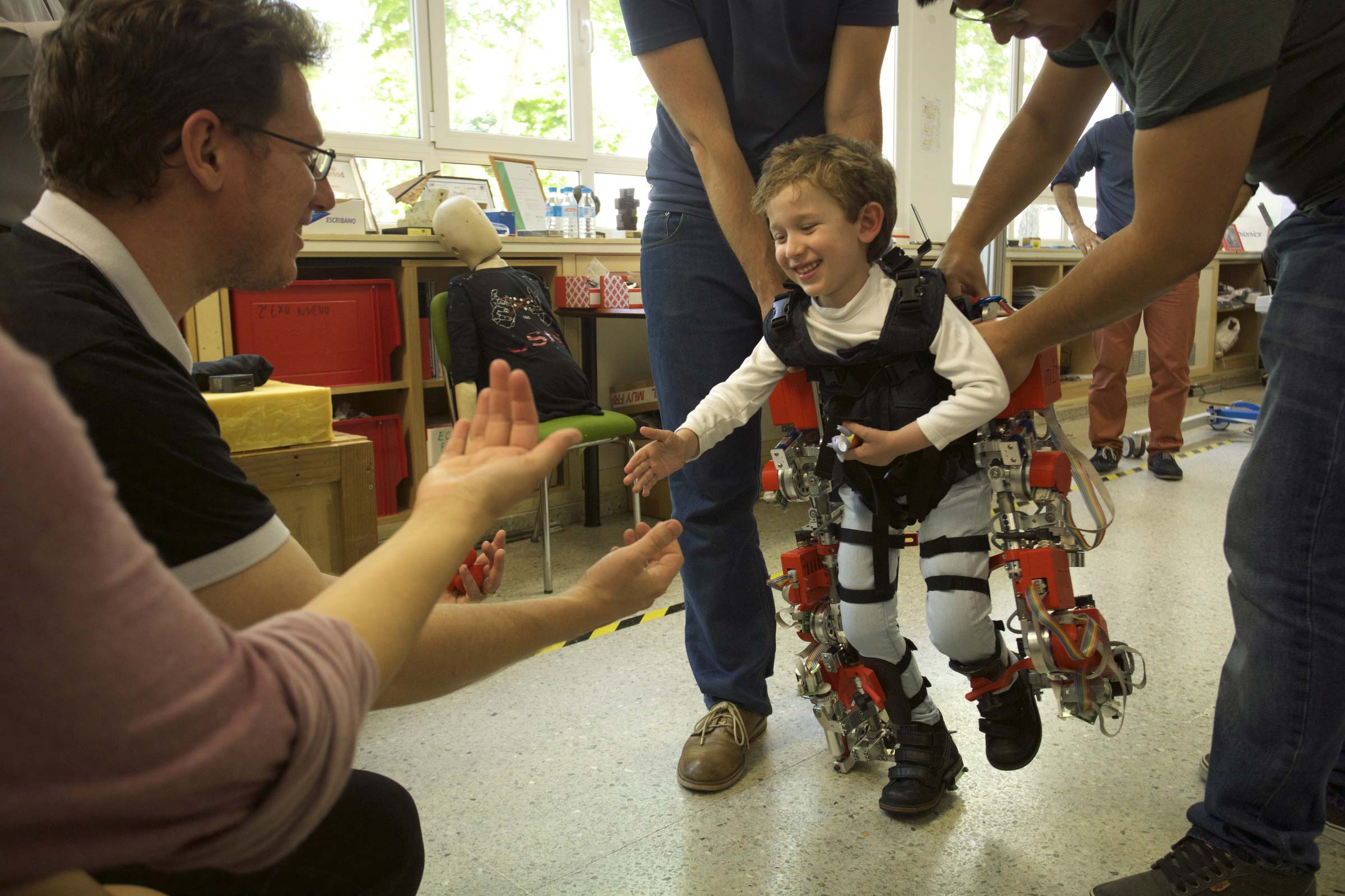 Imagen de Álvaro, de cinco años y afectado por atrofia muscular espinal, camina hacia sus padres durante una prueba del exoesqueleto. / Joan Costa