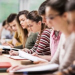 Group of students having a class. Focus is on young woman writing