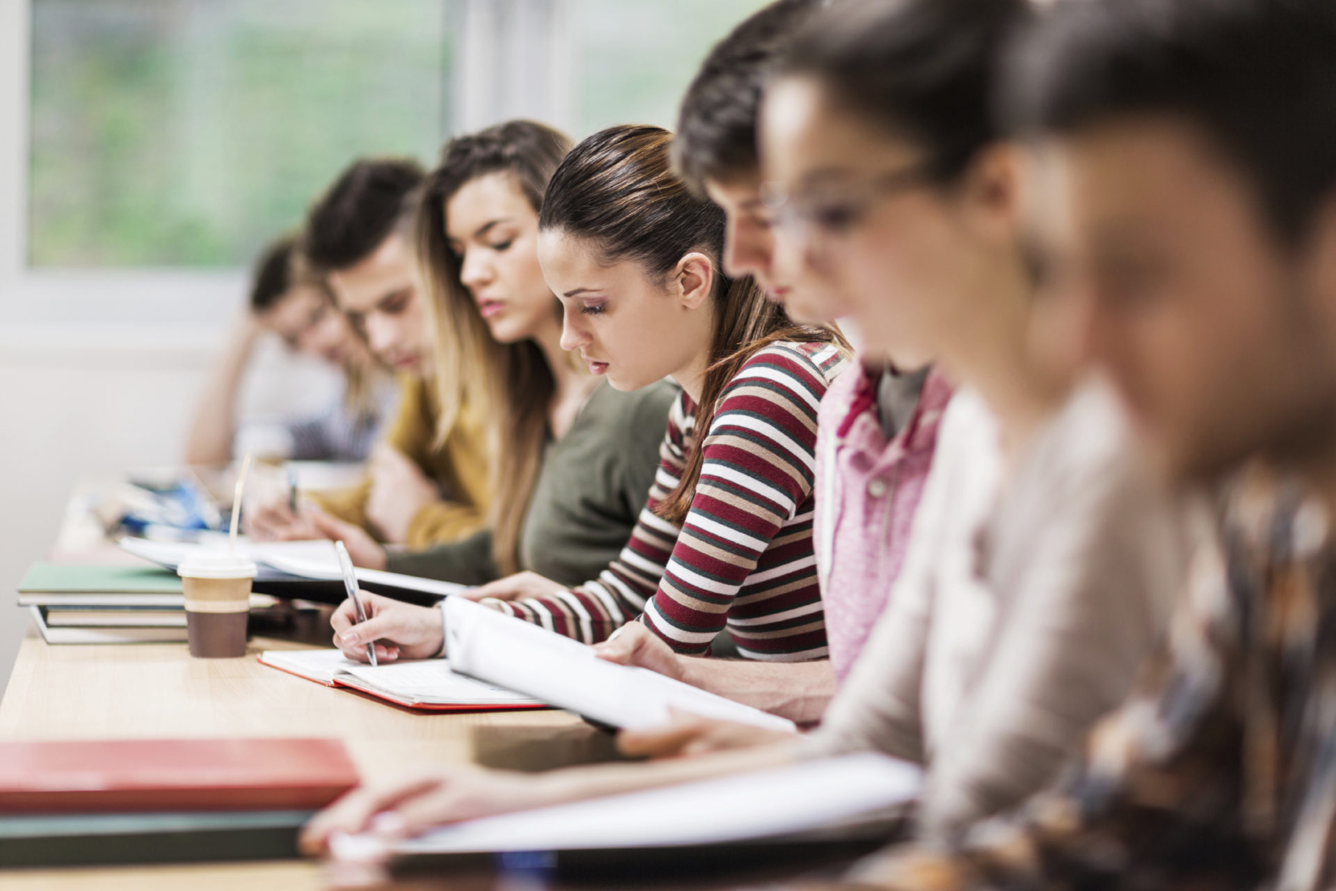 Group of students having a class. Focus is on young woman writing