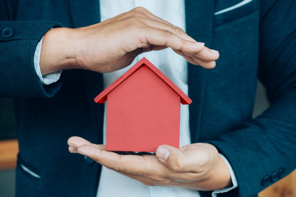 Business man hand hold the house model saving small house. seguro multiriesgo Business man hand hold the house model saving small house. seguro multiriesgo