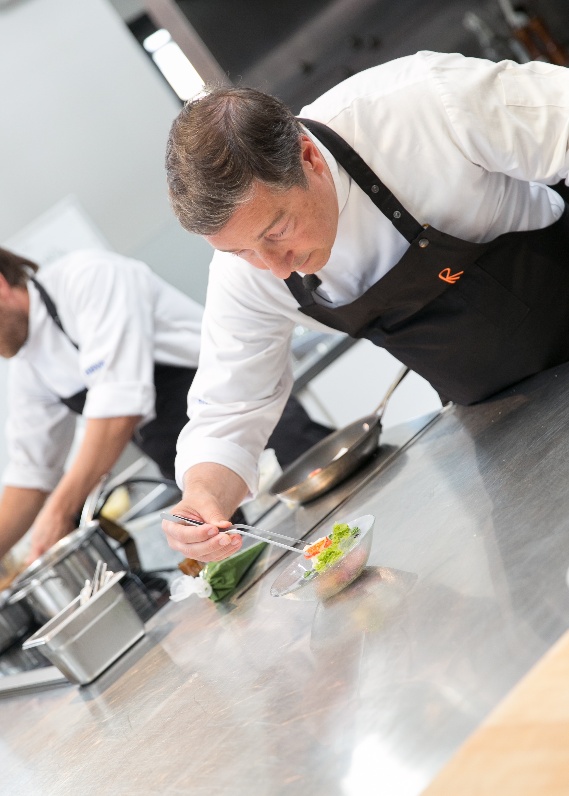 This is a photo of El Celler de Can Roca head chef Joan Roca plating Lobster Parmentier with Mole Sauce and Phytoplankton Sponge Cake Smoked with Spices at the San Francisco Cooking School master class. El Celler de Can Roca head chef Joan Roca plates Lobster Parmentier with Mole Sauce and Phytoplankton Sponge Cake Smoked with Spices.